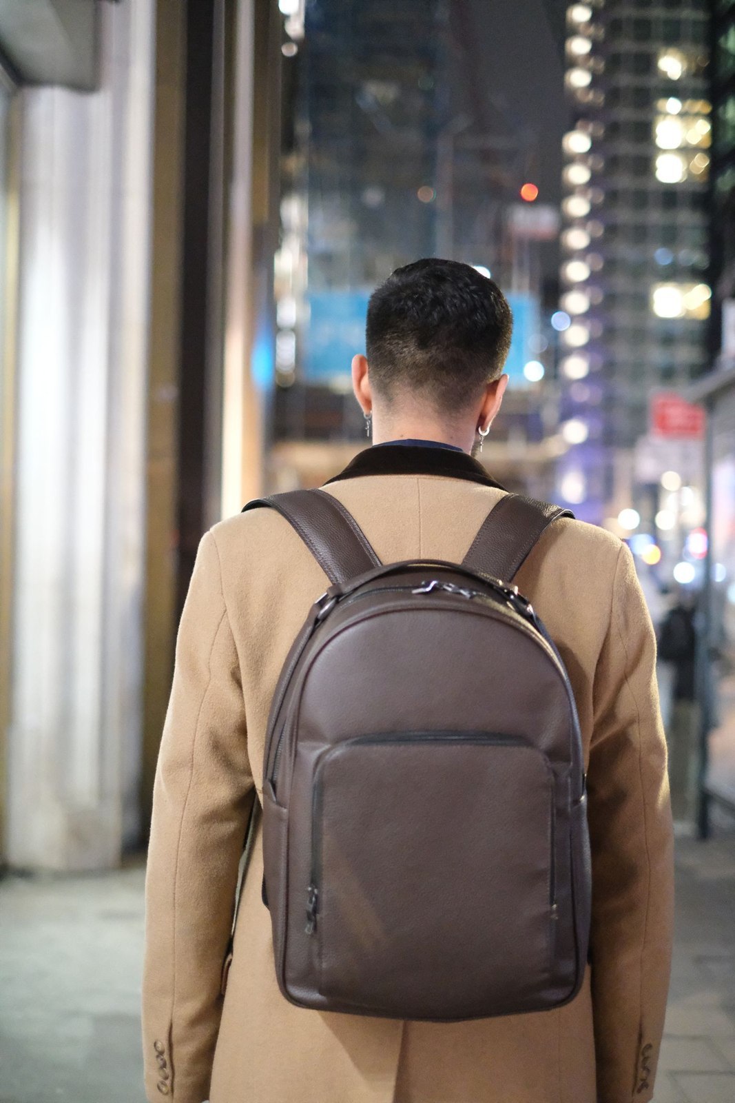 A compact backpack worn over a beige coat