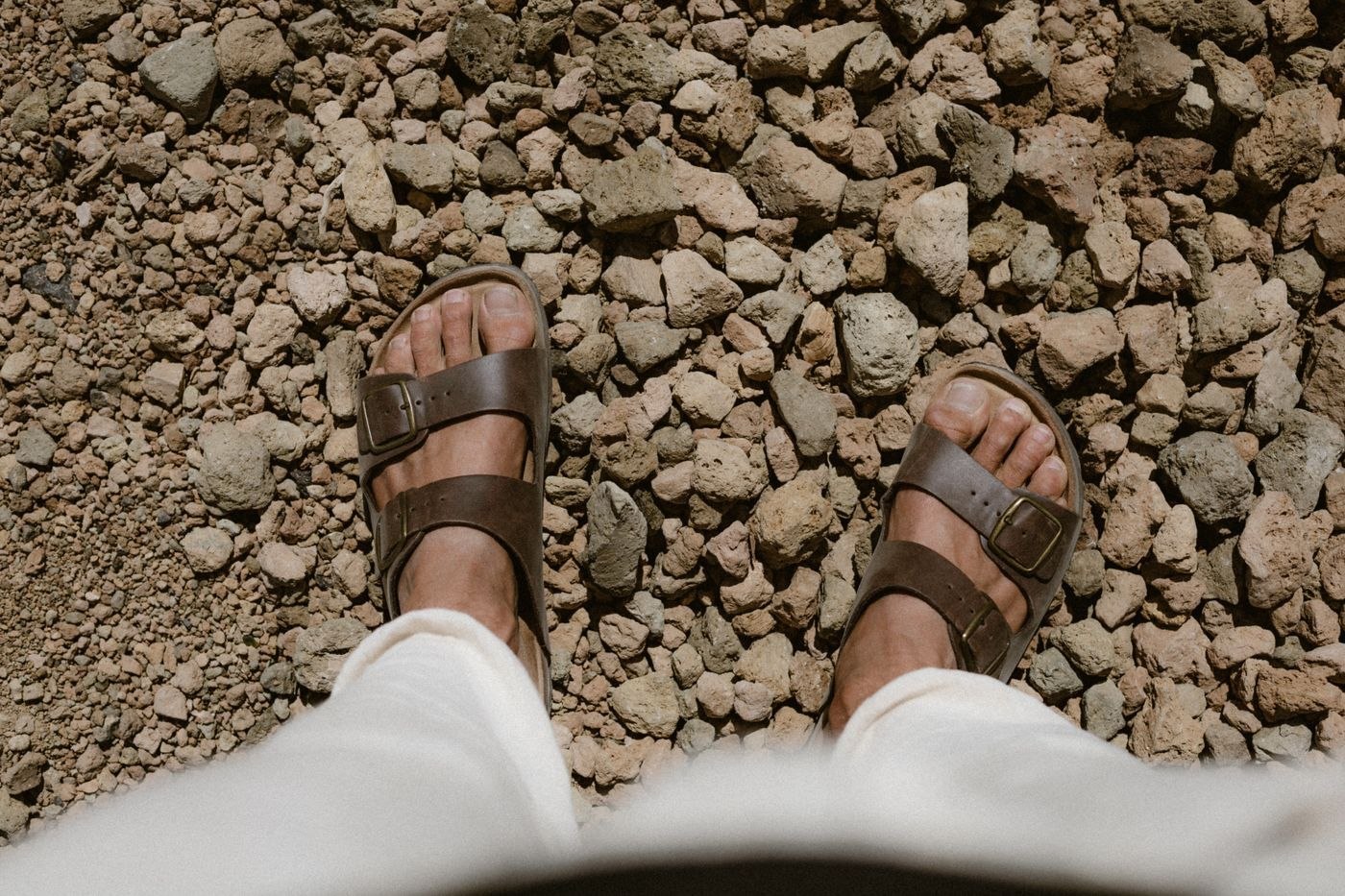Brown sandals beneath pale trousers
